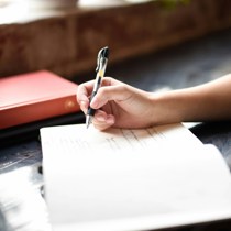 Photo credit Hannah Olinger via Unsplash - Photo of a hand writing in a journal as a strategy to quiet your mind at bedtime.